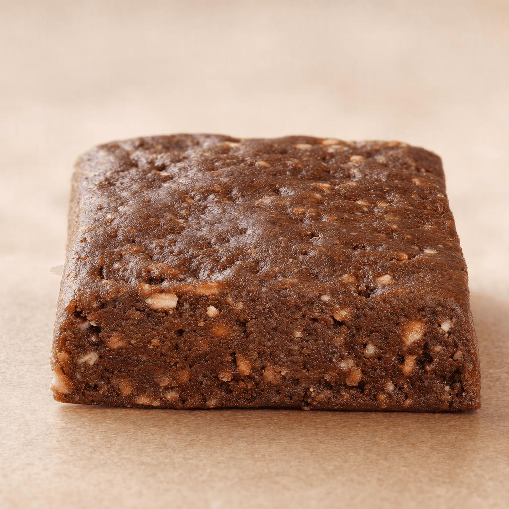 A compact, rectangular brown protein bar with a slightly uneven surface and a dense interior dotted with small lighter-colored pieces.