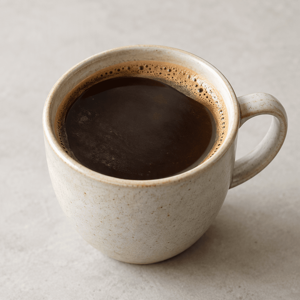 A dark brown coffee with a smooth surface and a thin layer of light brown foam, served in a cup.