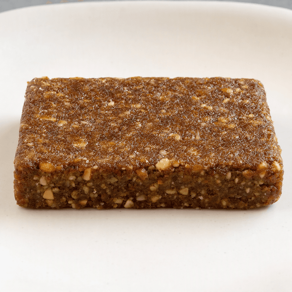 A compact, rectangular brown bar with a dense, slightly uneven surface and small visible pieces embedded throughout, shown whole on a plain plate.