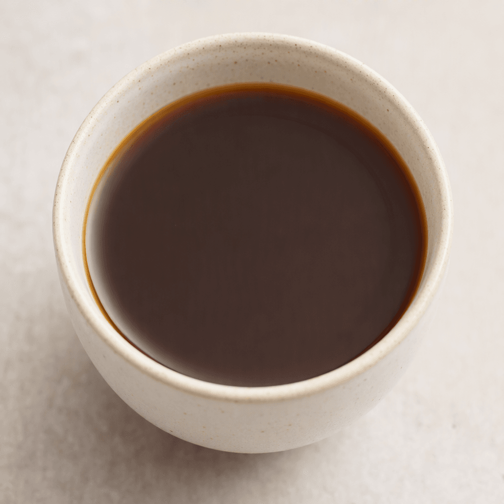 A dark brown, nearly black coffee with a smooth surface is served in a plain cup.