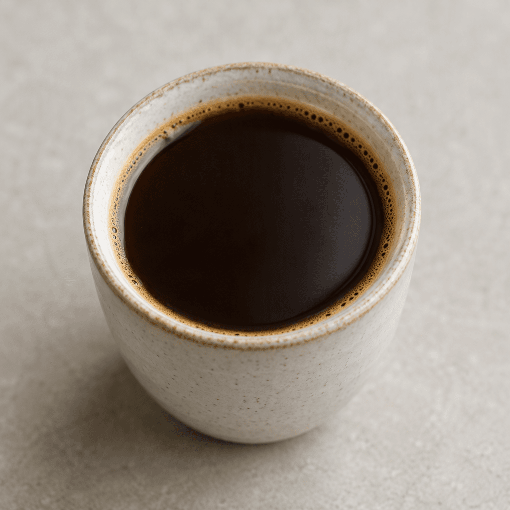 A small cup holds a smooth, nearly black-brown coffee with a faint tan ring of foam around the surface.