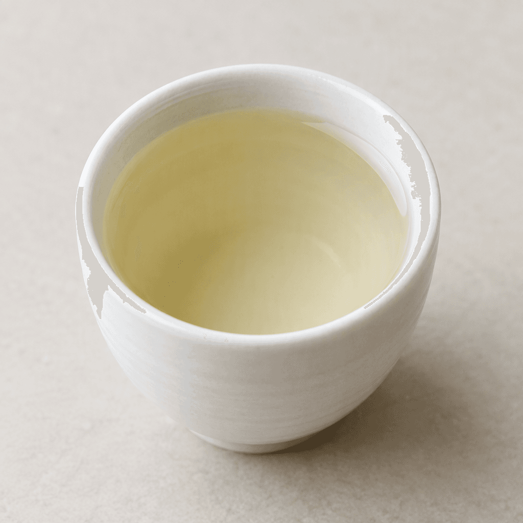 Clear, pale straw-coloured sake fills a small white ceramic cup, with a smooth, still surface.