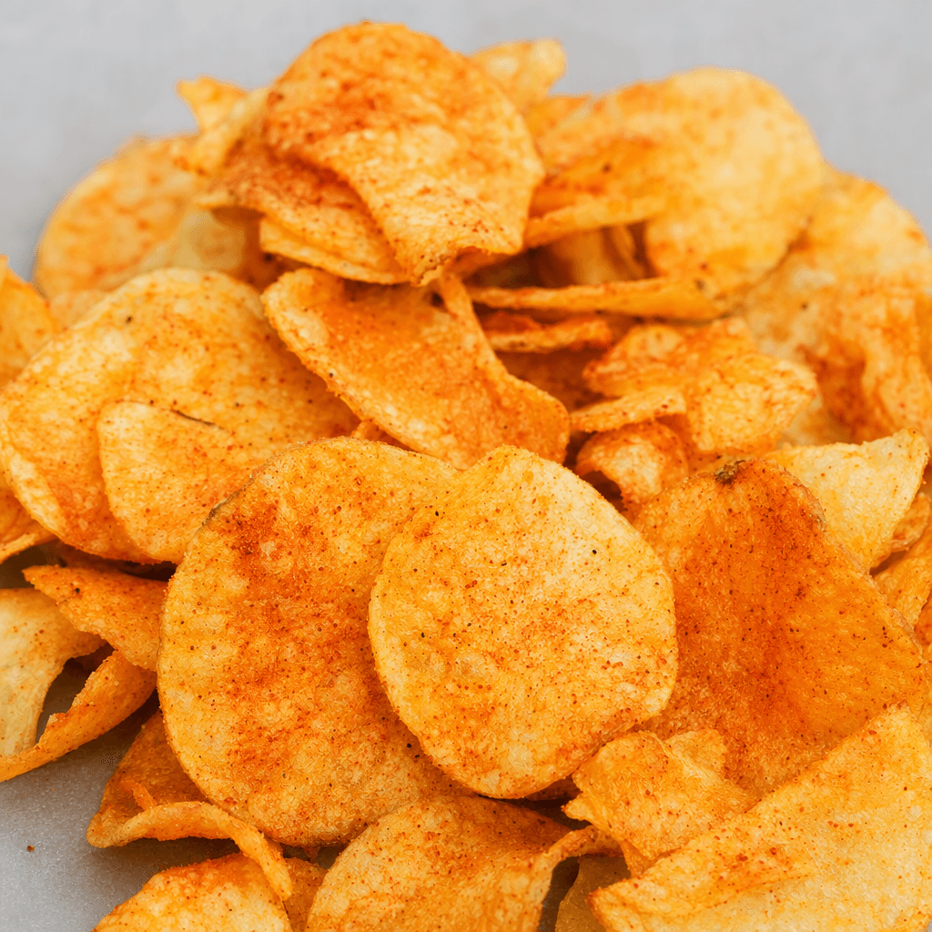 Thin, irregularly round potato chips with curled edges, a crisp blistered surface, and a golden-orange coating dotted with reddish spices, loosely scattered in a small pile.