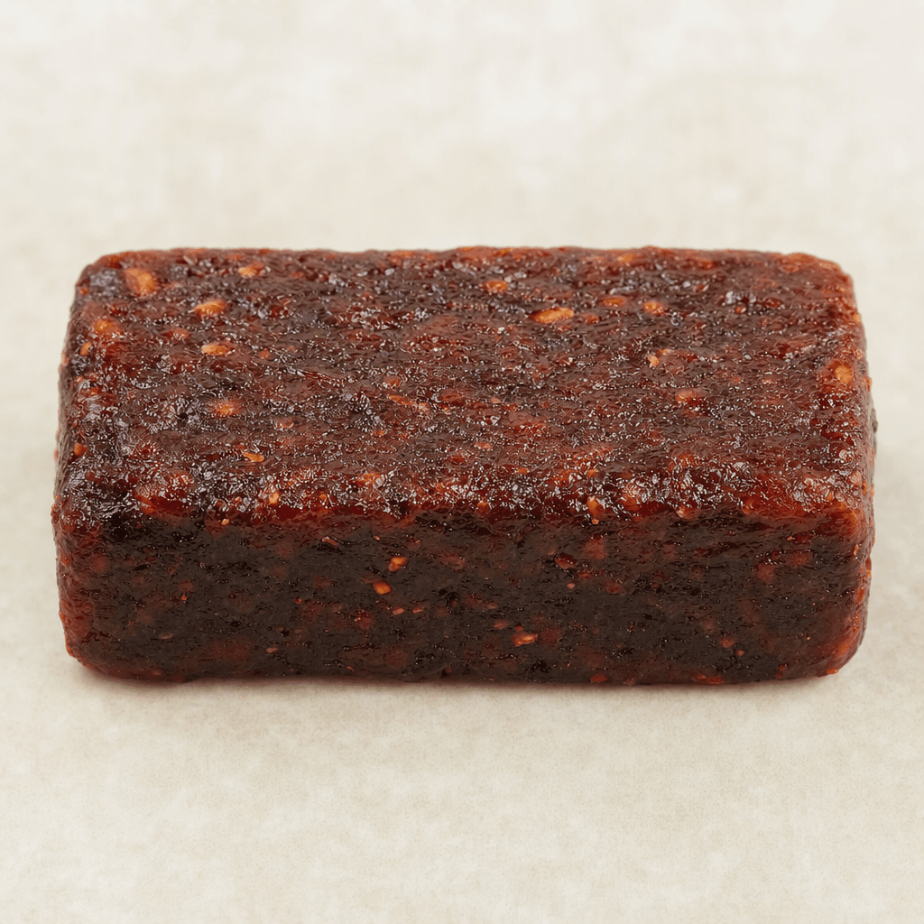 A small, compact rectangular fruit bar with a dark reddish-brown, slightly uneven and glossy surface, shown whole.