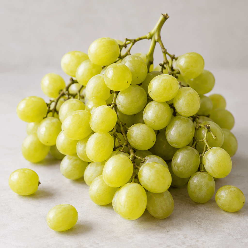 Small, round yellow-green grapes with smooth, slightly translucent skins hang in loose clusters, showing thin stems and a few scattered individual grapes on a clean surface.