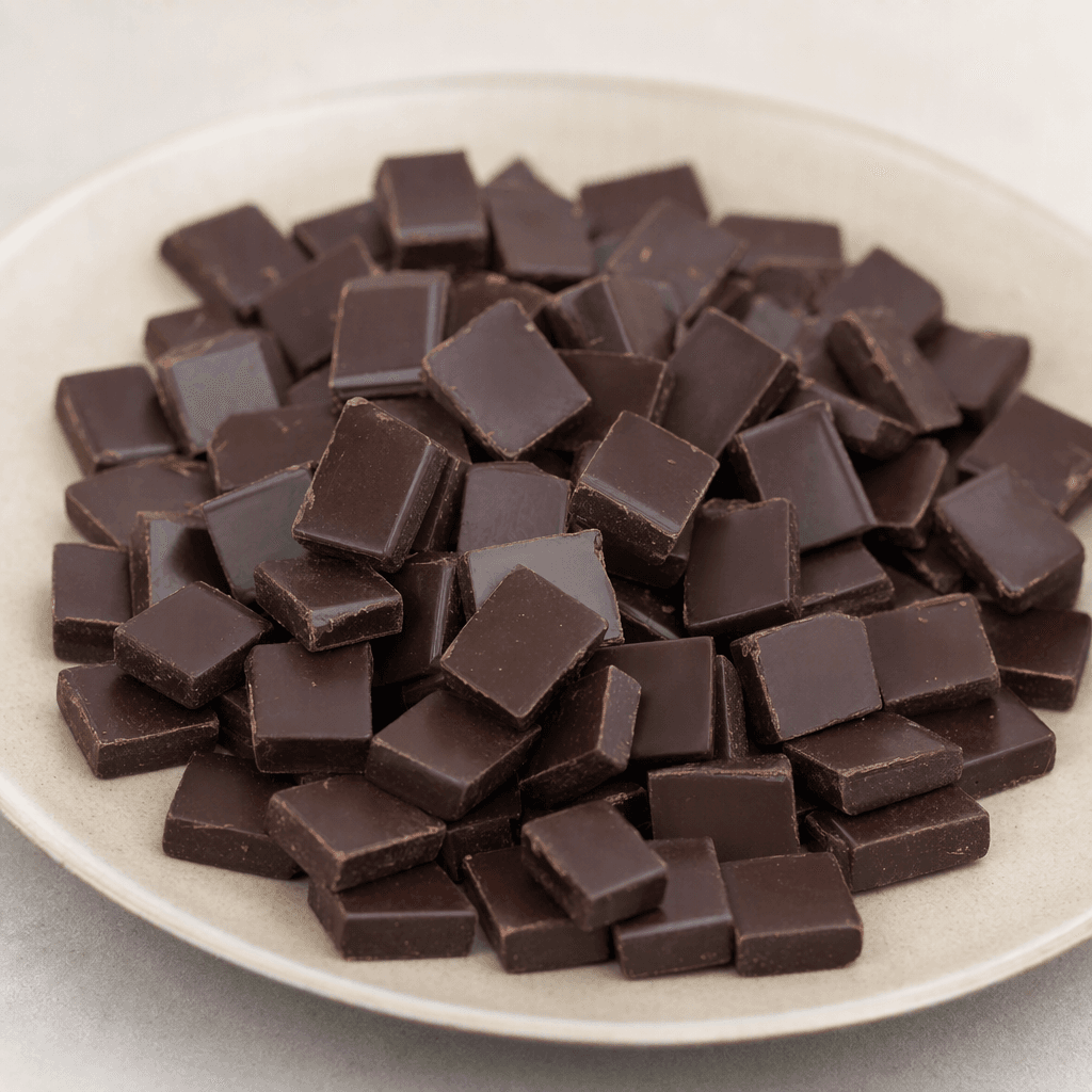 Small, bite-sized pieces of dark brown chocolate with smooth, slightly glossy surfaces and neat rectangular shapes, arranged together on a plain plate.