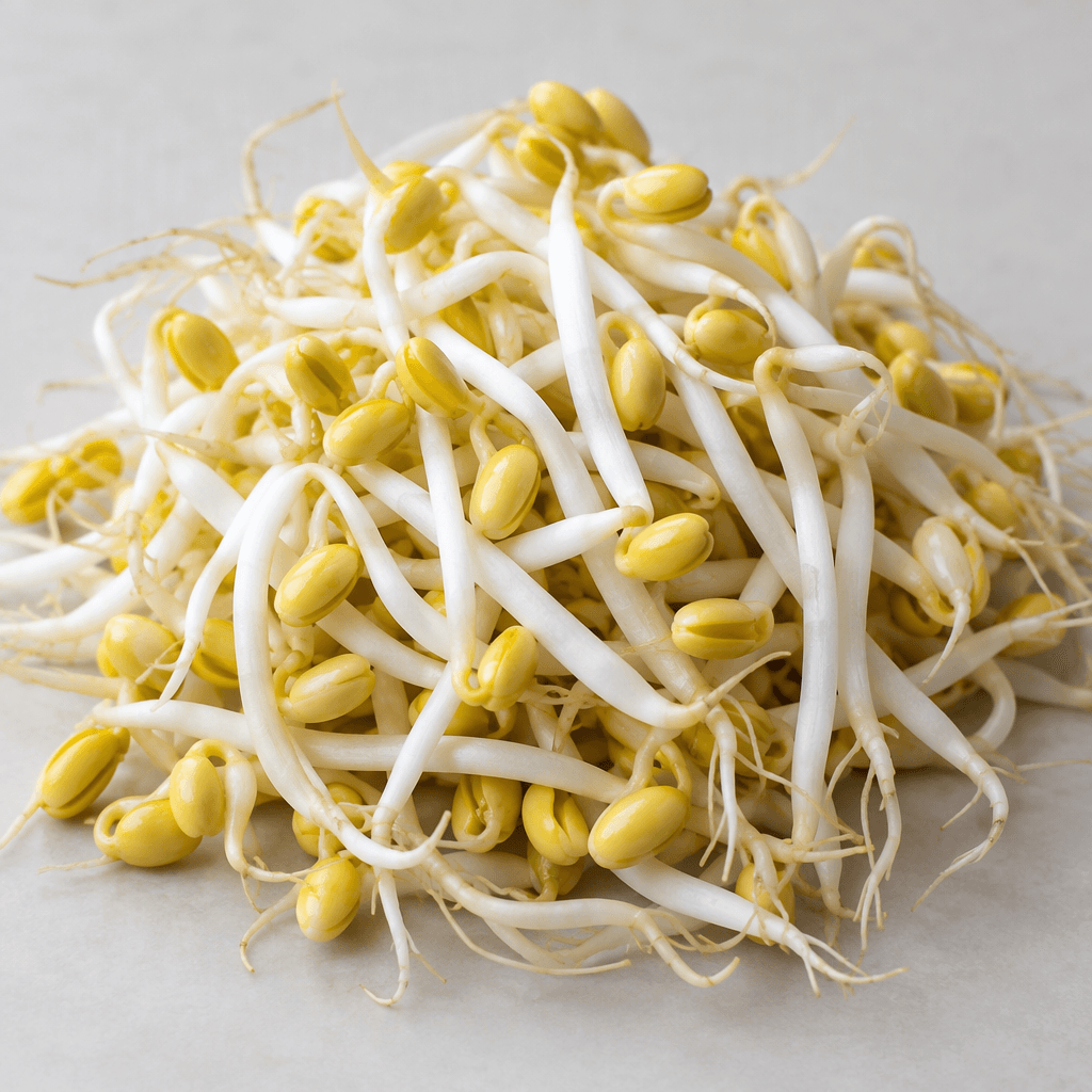 Pale cream-white sprouts with thick, crisp stems, small yellow bean-like seed heads, and fine tapering roots, loosely piled on a plain surface.
