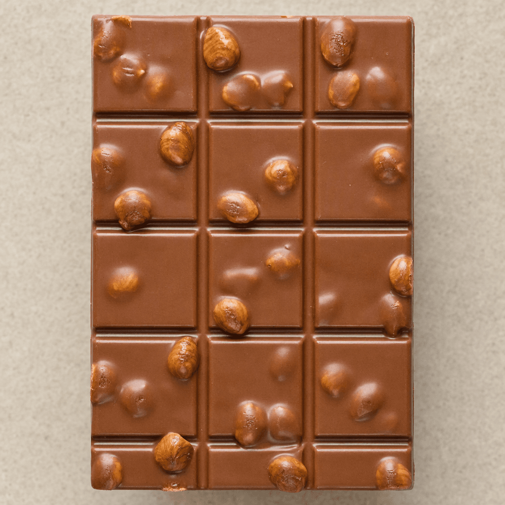 A rectangular milk-chocolate bar divided into small sections, with whole hazelnuts visible in its smooth, glossy brown surface.