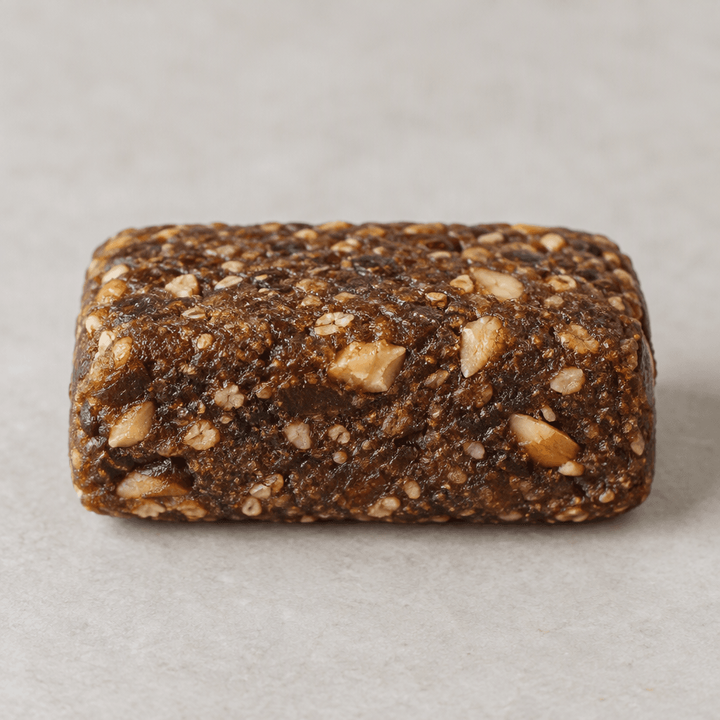 A compact, rectangular dark-brown bar with softly rounded edges, a slightly textured surface, and small pieces of pale tan nuts visible throughout.