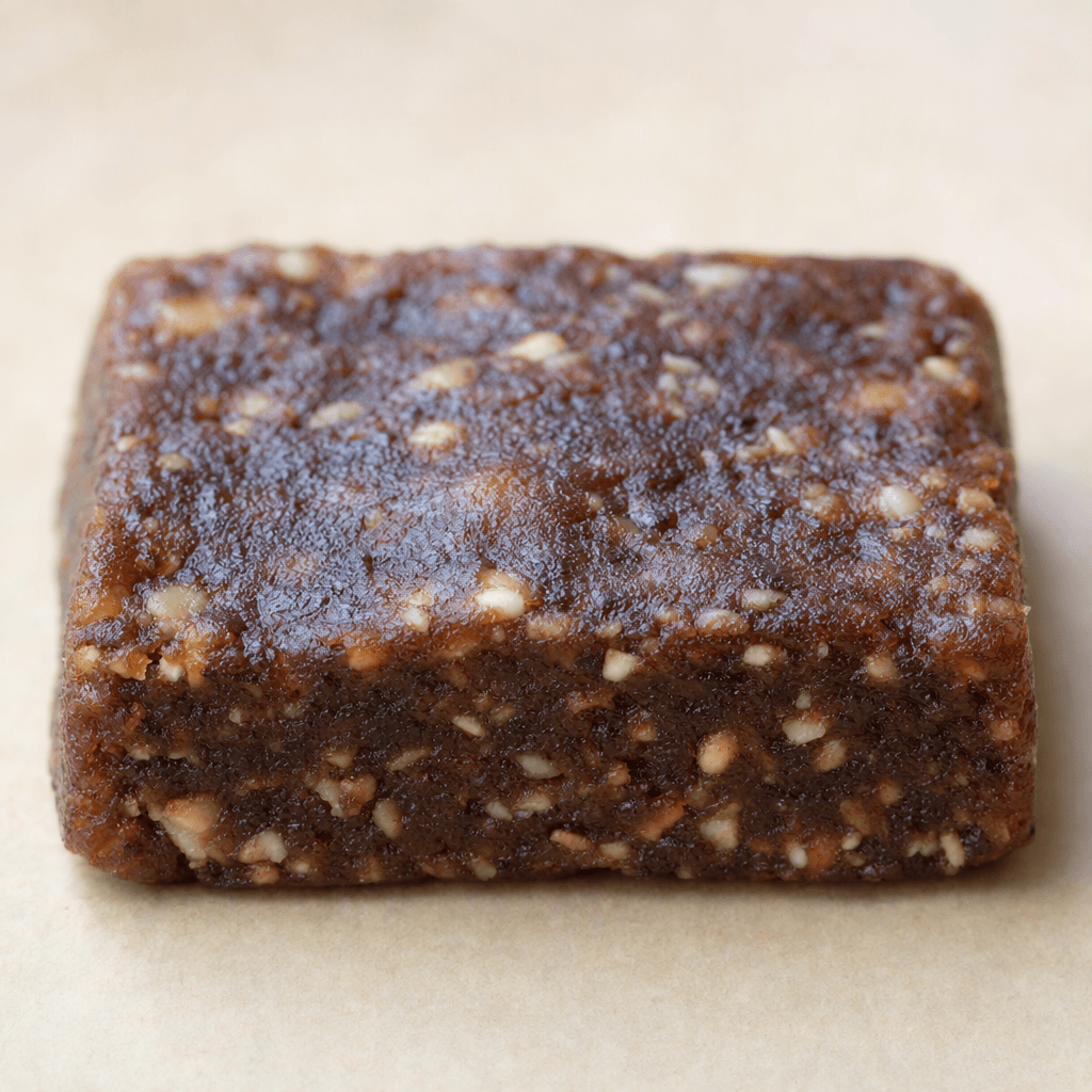 A compact, rectangular dark-brown bar with a slightly uneven surface and small pale pieces visible throughout, served on its own.