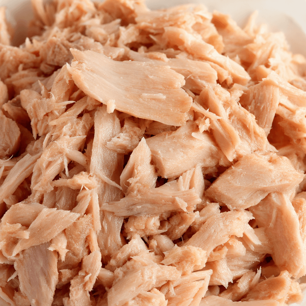 Pale pink-beige tuna appears in moist, loosely packed flakes and small irregular chunks, with no visible liquid.