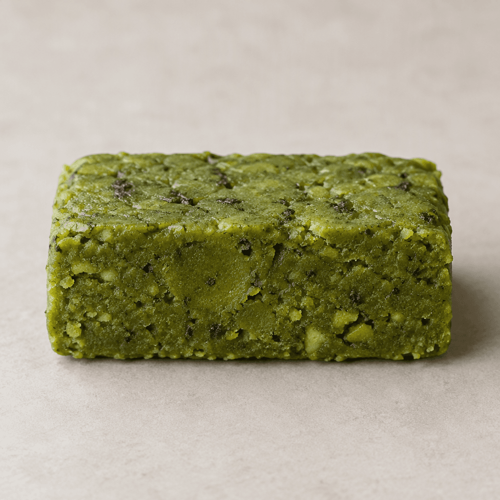 A compact, rectangular matcha-green bar with a dense, slightly uneven surface and small darker green flecks.