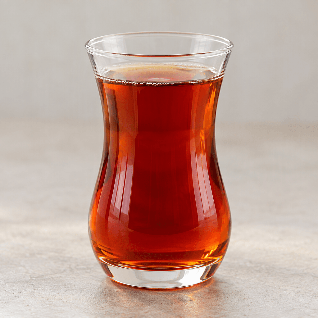 A clear, tulip-shaped glass holds deep reddish-amber tea, with the light shining through its smooth surface.