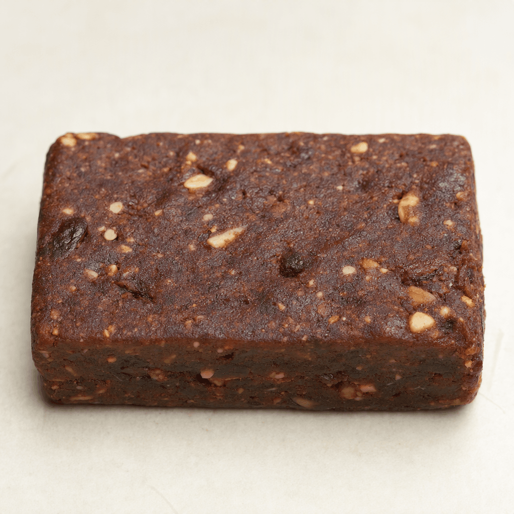 A compact, rectangular dark-brown bar with a slightly uneven, matte surface and small lighter-colored pieces visible throughout, shown whole on a plain surface.