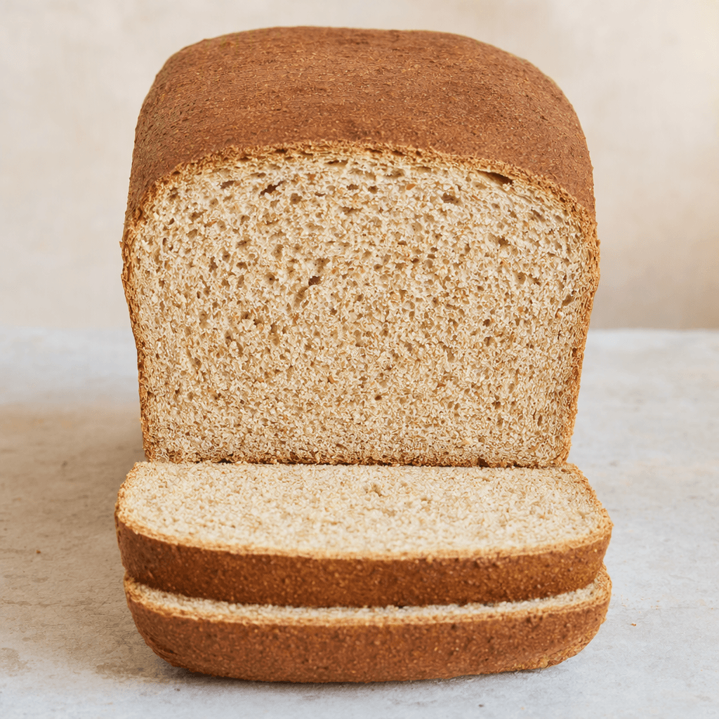 A rectangular whole-wheat loaf with a medium-brown crust and soft, light-brown sliced interior dotted with small wheat-bran flecks.
