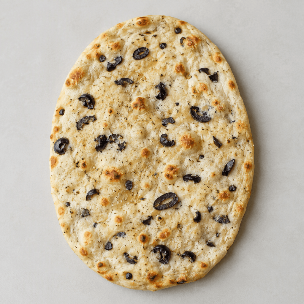 A thin, flexible, oval flatbread with scattered dark olive pieces and small golden-brown toasted spots across its pale surface.
