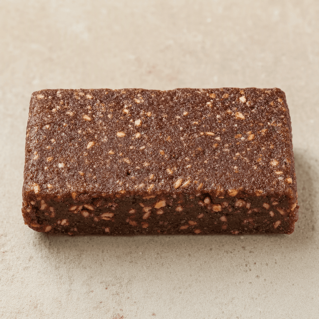 A compact, rectangular cocoa-brown protein bar with a dense, slightly grainy surface and subtly uneven edges.