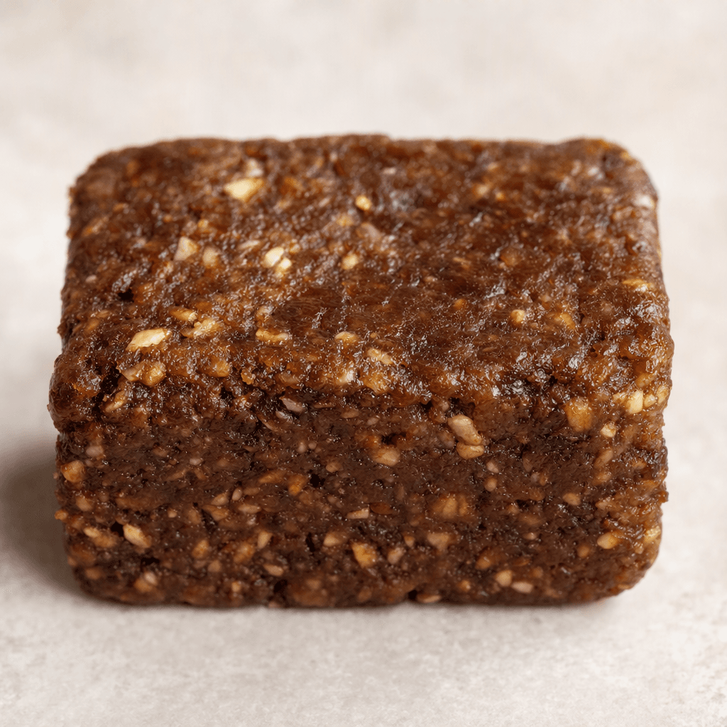 A small, roughly rectangular brown bar with an uneven, compact surface and a few visible grain-like flecks.