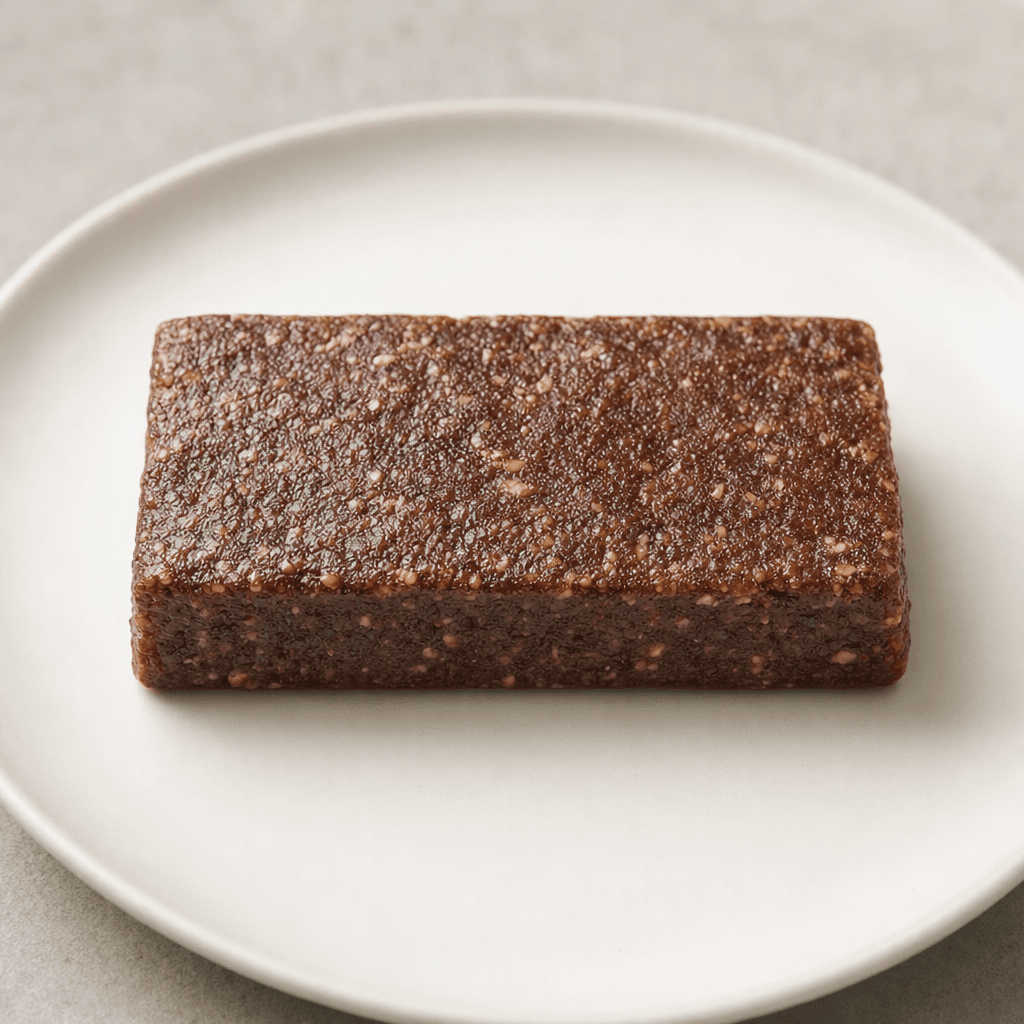 A compact, rectangular brown bar with a dense, slightly uneven surface, shown whole on a plain plate.