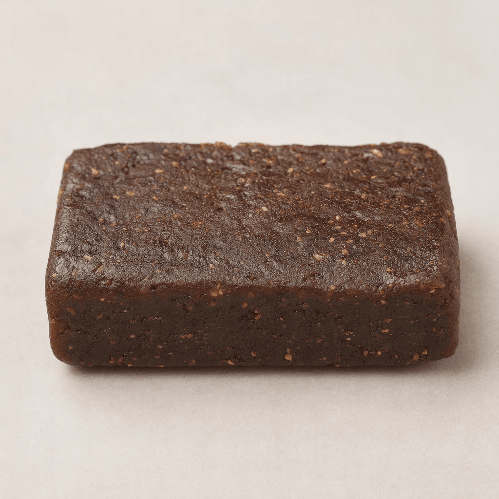 A compact rectangular dark-brown bar with a slightly uneven, dense-looking surface and small visible flecks, shown whole.