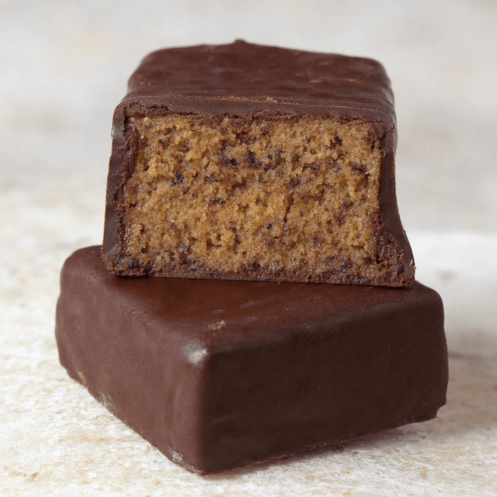 A compact, rectangular bar with a dark brown coating and a dense, light-brown interior dotted with small darker flecks, shown whole beside a cut piece.