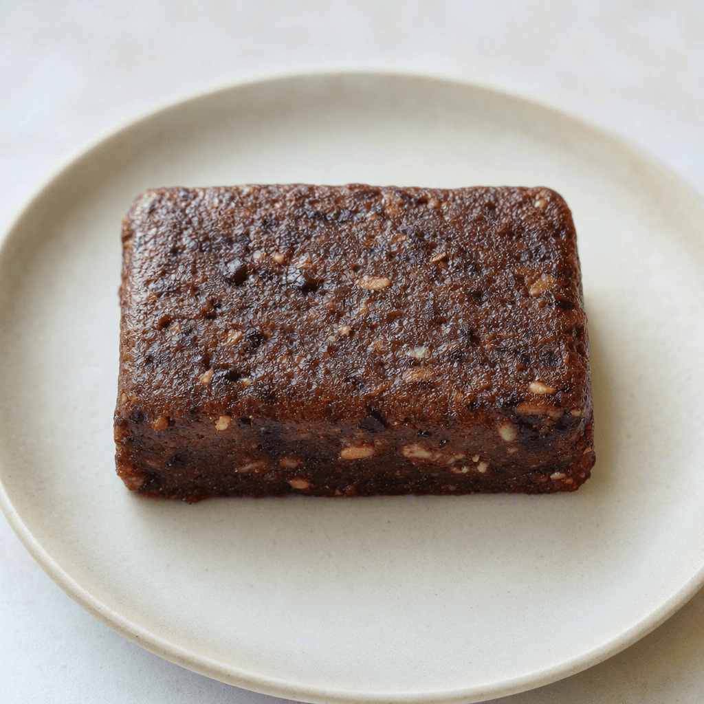 A compact, rectangular dark-brown bar with a dense, slightly uneven surface, shown on a plain plate.