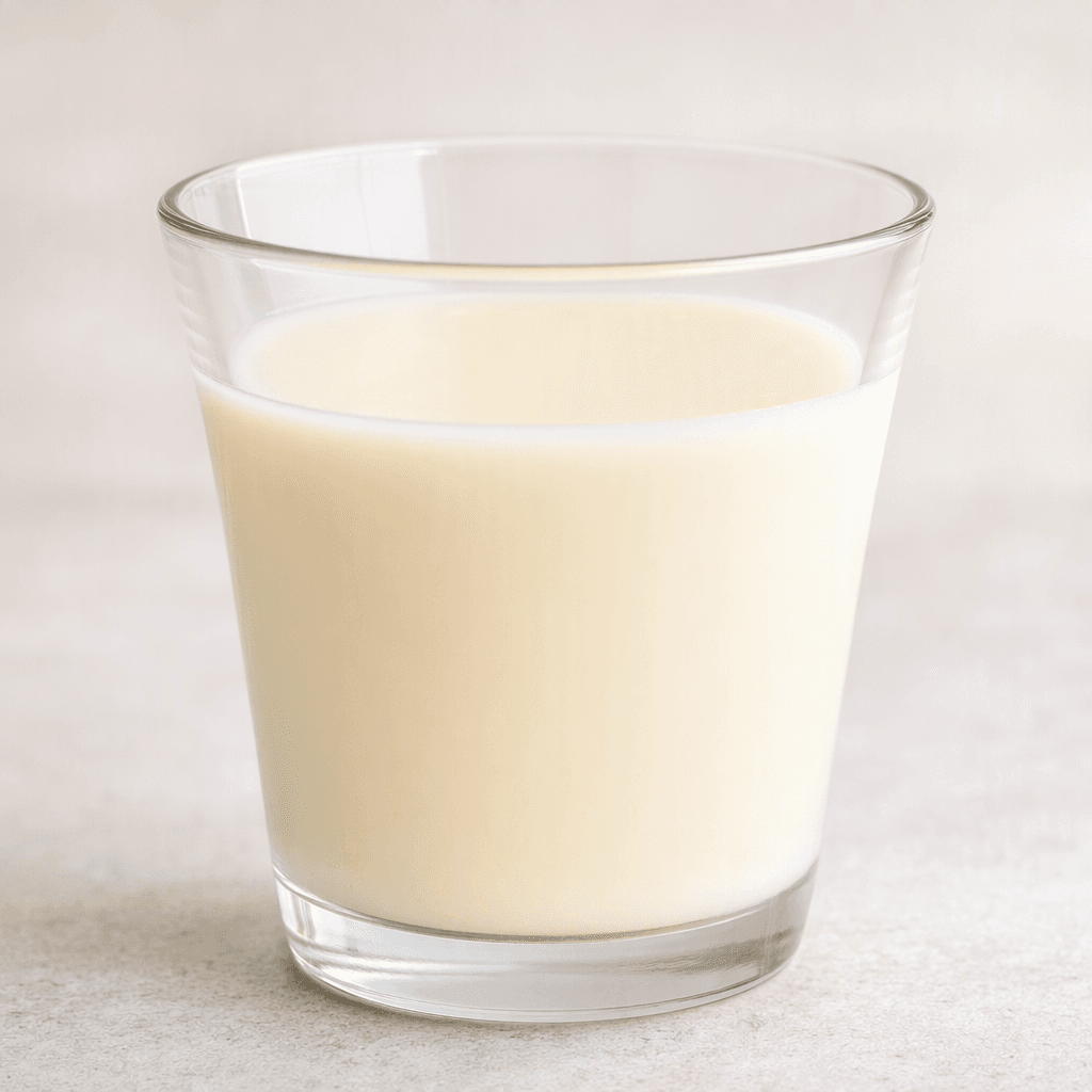 A small serving of smooth, opaque, pale ivory fermented milk drink sits in a clear glass.