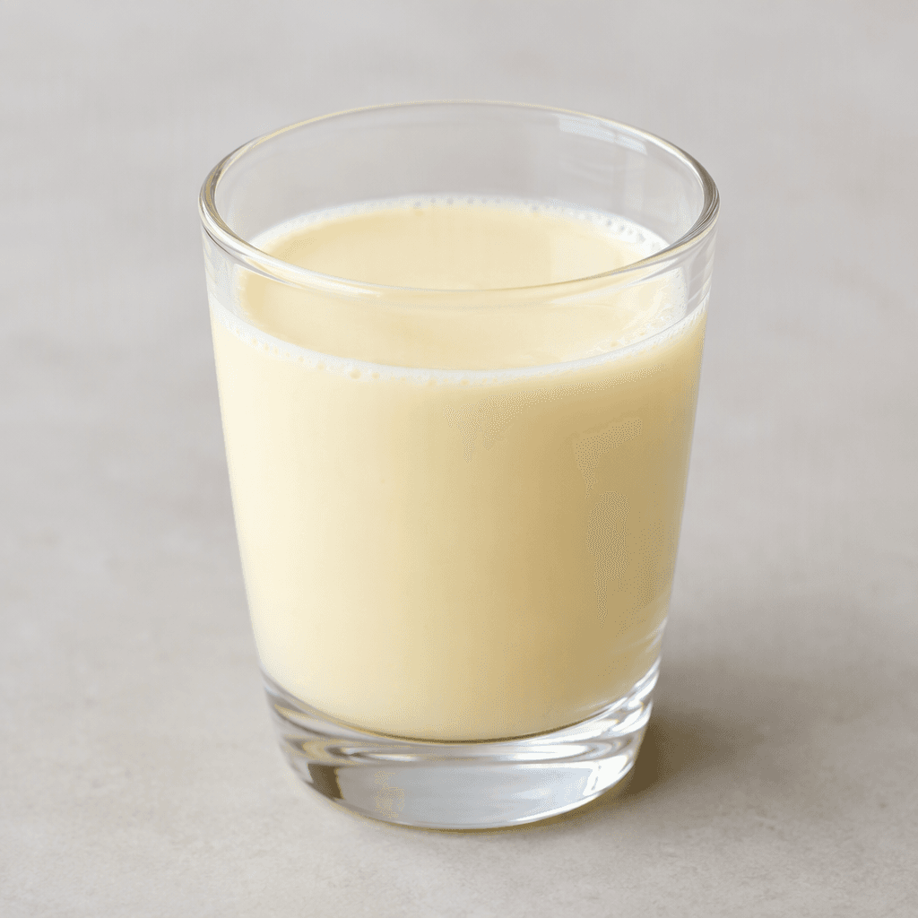 A small serving of smooth, opaque, pale cream-yellow probiotic milk drink sits in a clear glass.