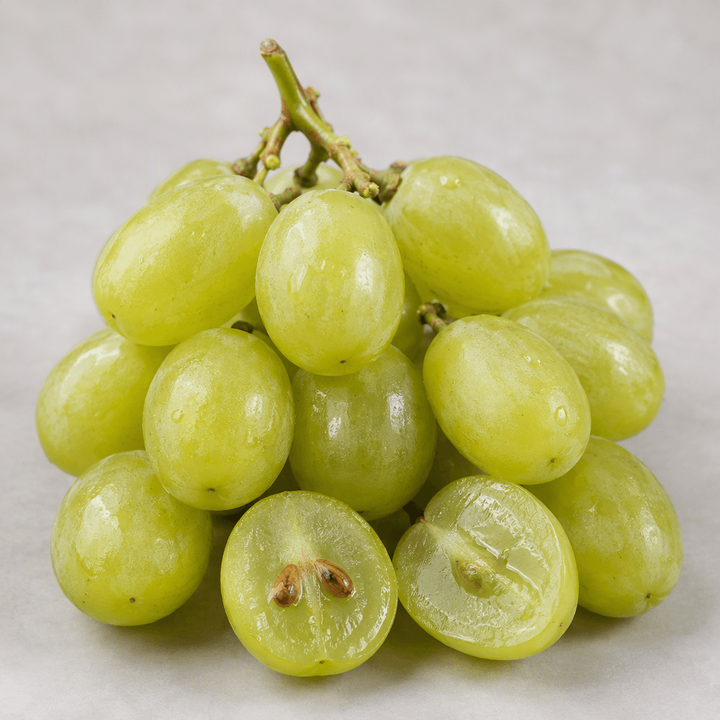 A small bunch of pale green, round-to-oval grapes with smooth, slightly translucent skins, firm stems, and a few grapes cut open to reveal their brown seeds and juicy translucent flesh.