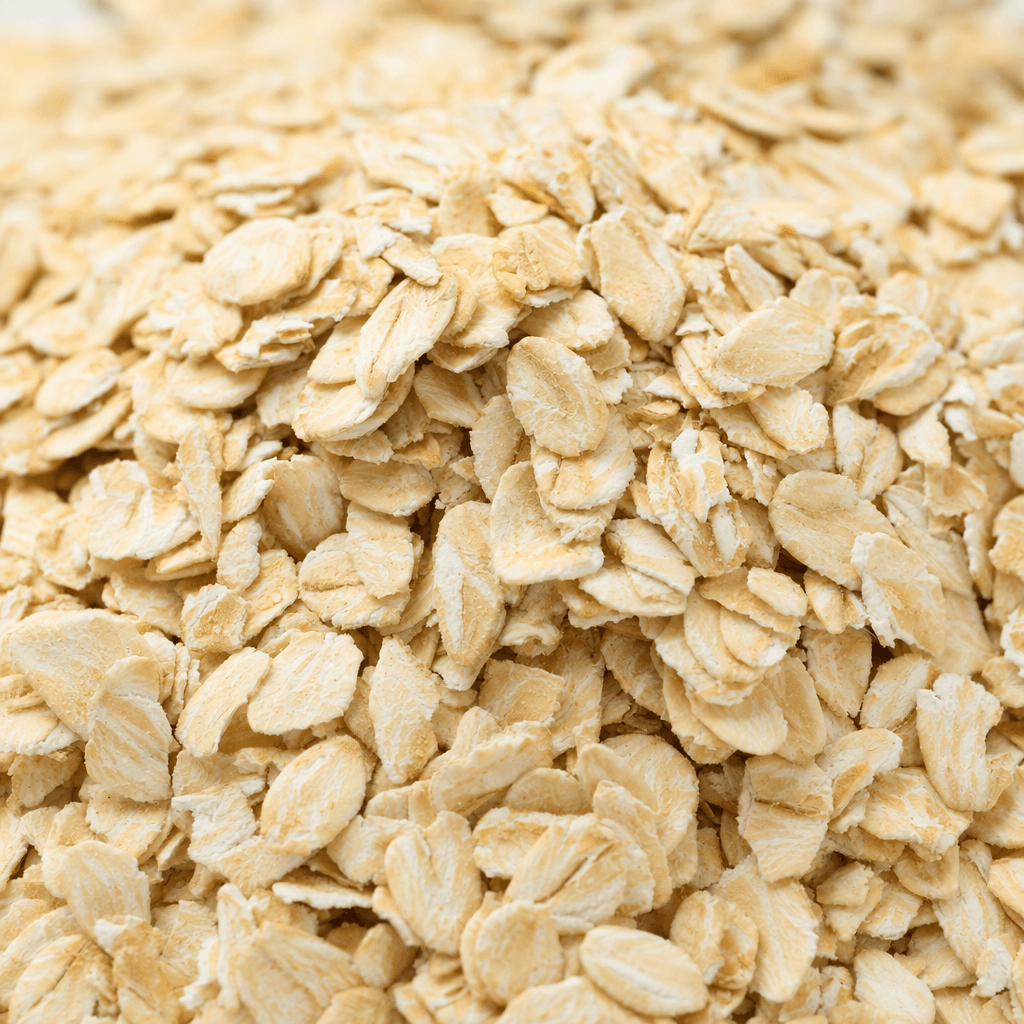 Loose, dry oat flakes are pale beige with a matte, slightly rough surface and thin, flattened, irregular oval shapes.