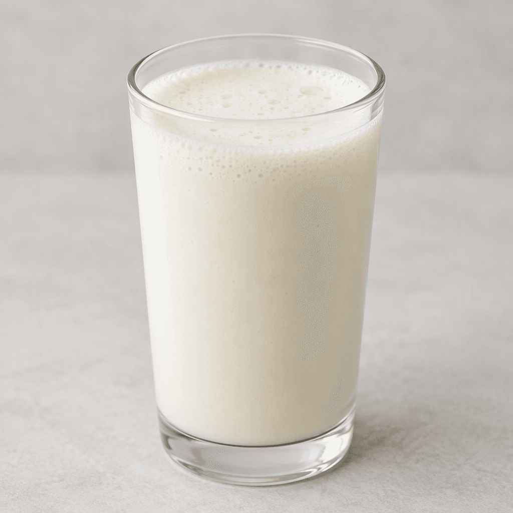 A smooth, pale ivory egg white protein drink sits in a clear glass, with a lightly foamy surface and a few tiny bubbles.