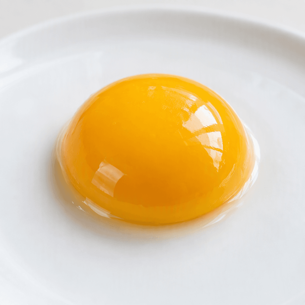 A single glossy, golden-yellow egg yolk with a smooth, slightly domed surface sits intact on a plain white plate.