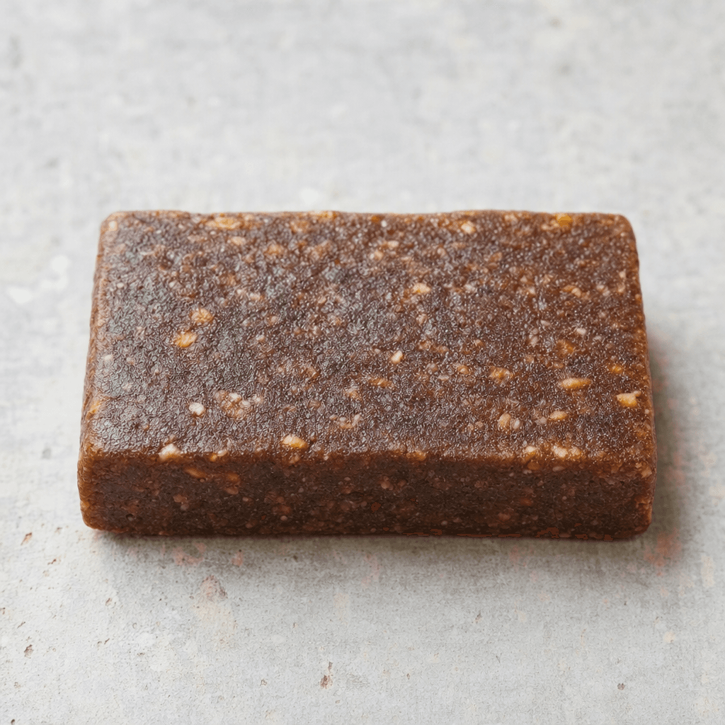 A small, dense rectangular fruit bar with a matte, deep brown surface and tiny lighter flecks, shown whole.